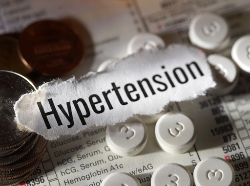 Hypertension text on a medical chart surrounded by white tablets and coins.