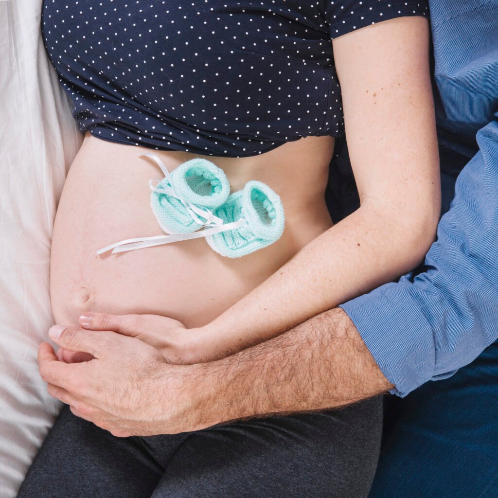 Pregnant woman holding a heart-shaped cushion on her belly with an ultrasound image nearby, representing maternal kidney care.